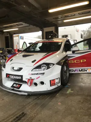 White and red touring race car, front view, in the pit garage